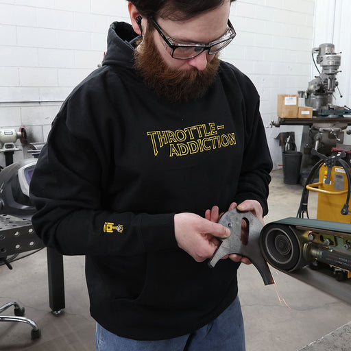 Man grinding a piece of metal wearing a black throttle addiction embroidered hoodie
