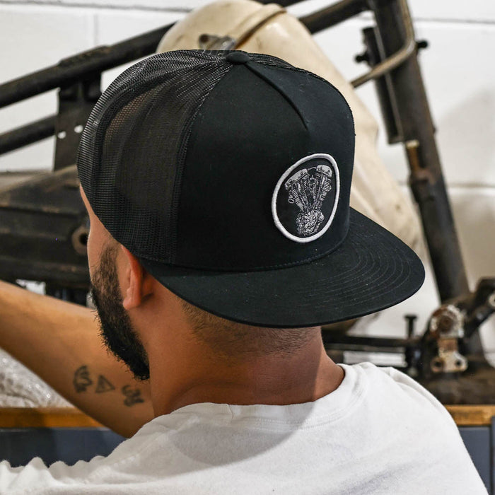 Person wearing a black cap with a logo, sitting in a casual setting.
