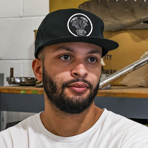 Man wearing a black cap with a logo in a kitchen setting