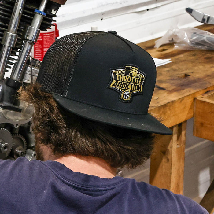 Person wearing a black cap with 'Throttle Addiction' logo in a workshop setting