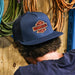 Person wearing a navy blue cap with a logo against a wooden background with coiled hoses.