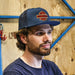 Man wearing a navy blue cap with a logo against a wooden background