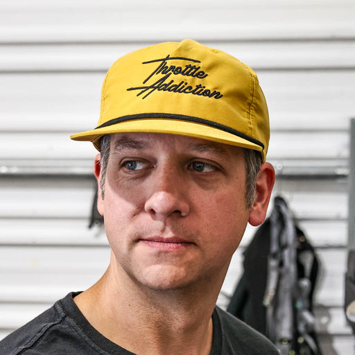 Man wearing a yellow cap with 'Throttle Addiction' text against a metallic background