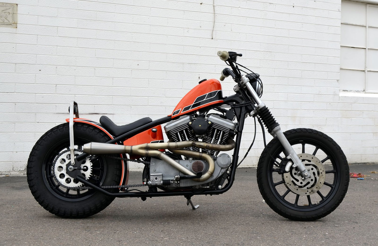 orange evo sportster weld on hardtail chopper in front of white brick wall
