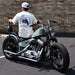 Man wearing a 'Thrill is Addiction' t-shirt standing next to a custom motorcycle against a brick wall.