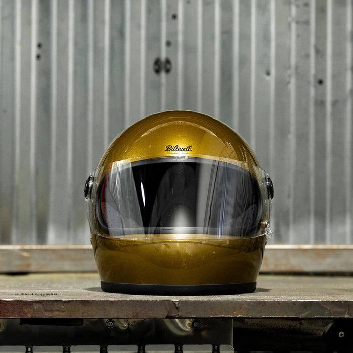 Gold helmet with clear visor on a wooden surface against a metal wall.