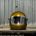 Gold helmet with clear visor on a wooden surface against a metal wall.