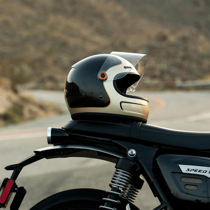 Champagne and charcoal helmet on a motorcycle with a blurred road and mountains in the background